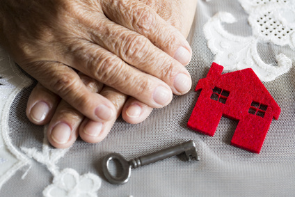 Red house, key, and wrinkled hands on a grey background in Dallas, TX